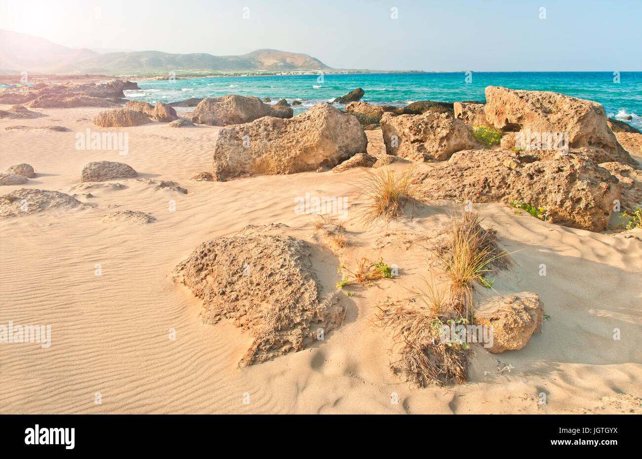 Falasarna beach a sunrise con rocce e le piante in primo piano e le montagne a sfondo su cancella il giorno di estate, Creta, Grecia Foto Stock