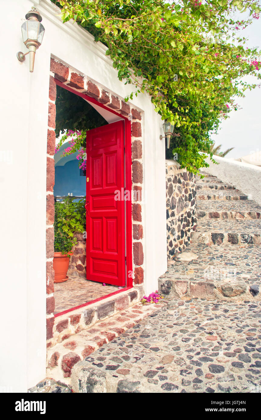 Rosso di aprire la porta di una casa con la rigogliosa pianta su di esso sulla calda giornata di primavera con scale di boulder in Oia - Santorini o Thira, Grecia Foto Stock