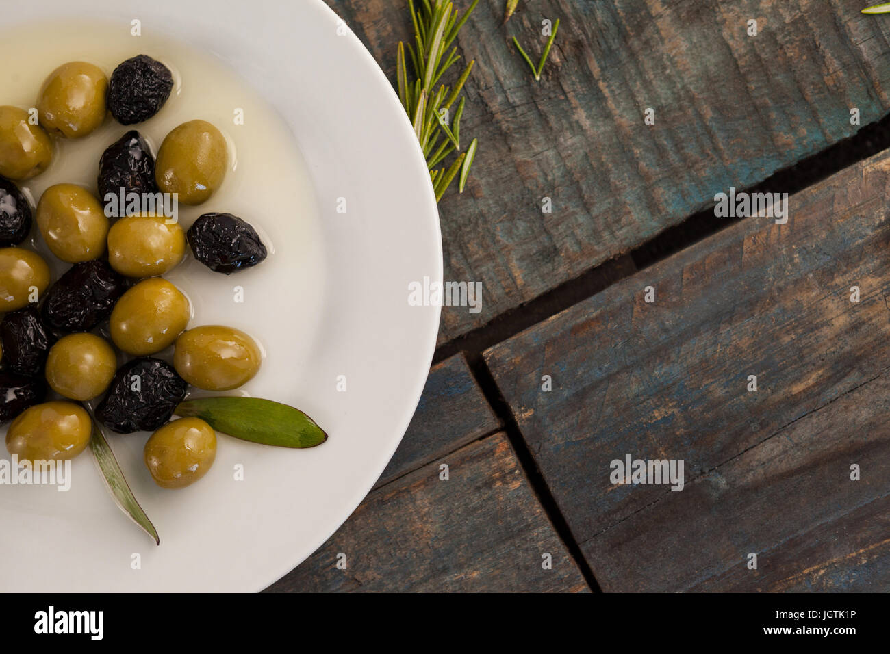 Vista aerea del verde e secca di olive nere con olio nella piastra sulla tavola di legno Foto Stock