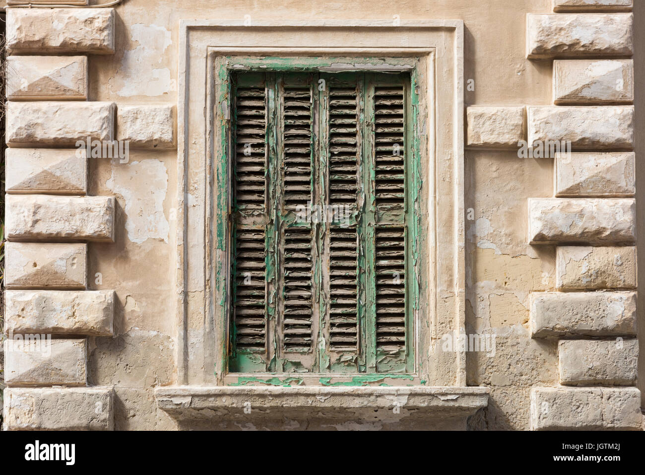 Una vecchia finestra ritagliata su un edificio in Malta con peeling vernice verde Foto Stock