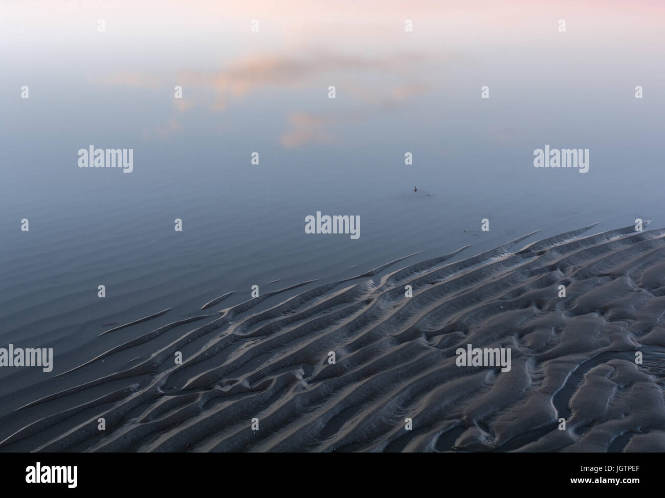 Riflessioni di drifting nuvole rimbalzare acqua liscia increspata sulla spiaggia Foto Stock