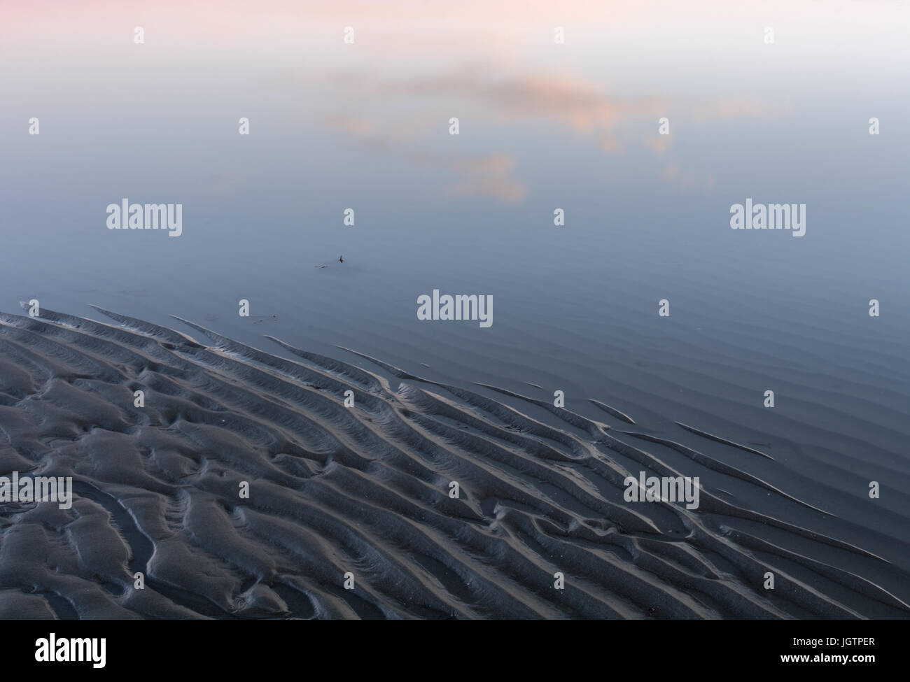 Riflessioni di drifting nuvole rimbalzare acqua liscia increspata sulla spiaggia Foto Stock