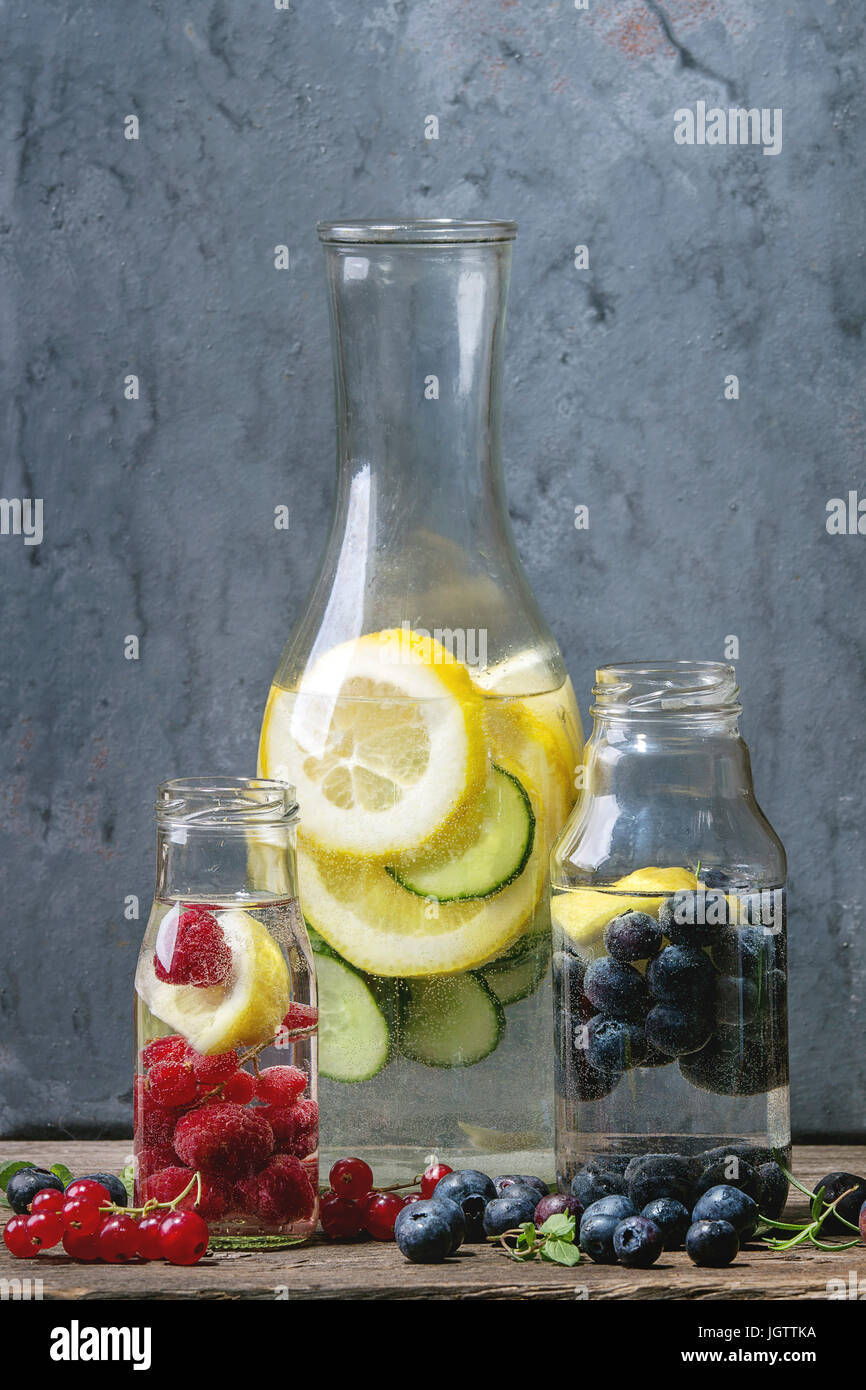 Cetriolo di agrumi bacche Mirtilli e rasberry sassy sassi acqua per detox in bottiglie di vetro di legno su sfondo blu. Pulire mangiare, uno stile di vita sano Foto Stock