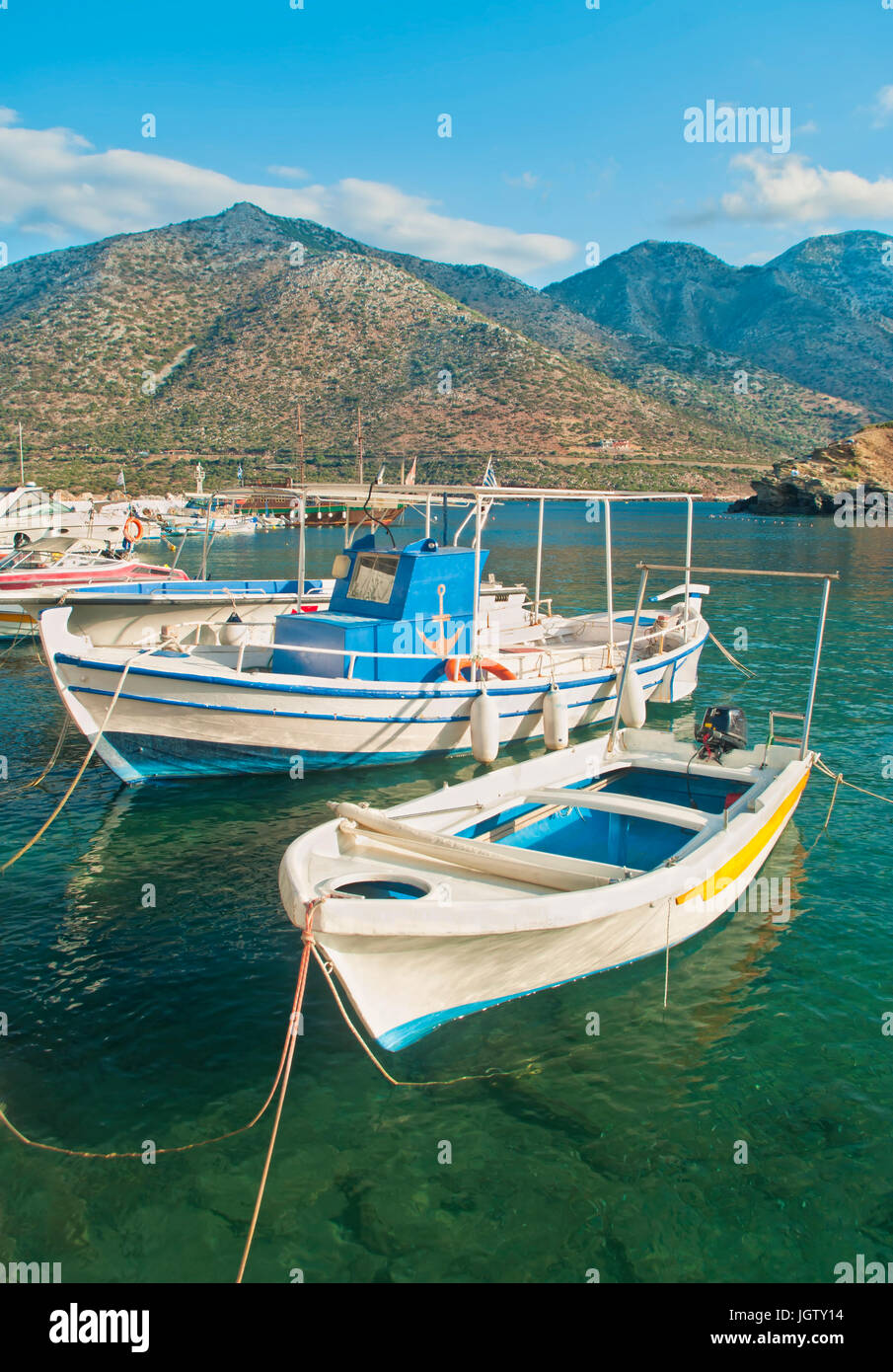 Bianco di piccole barche a motore ormeggiata presso il molo nel villaggio cretese di Bali circondato da montagne di sunny sera, Creta, Grecia Foto Stock