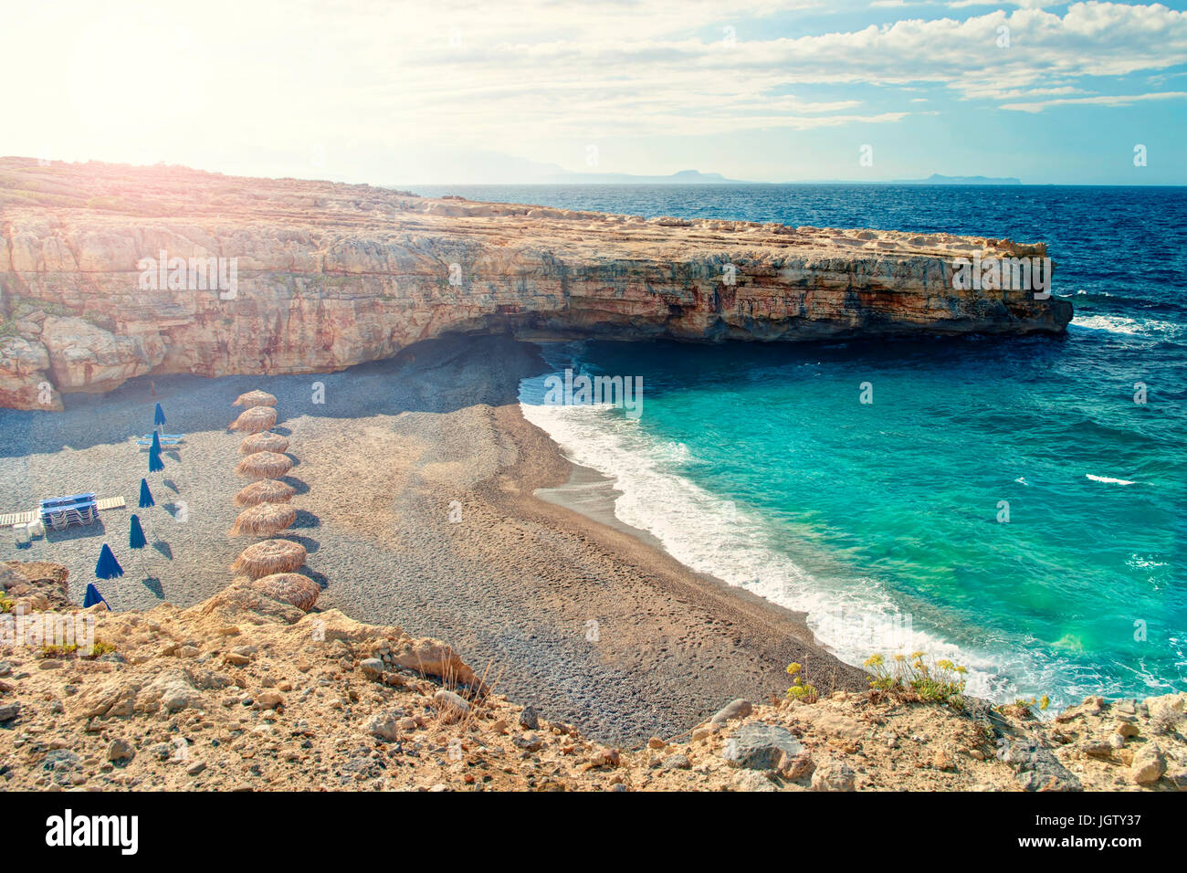 Cross-immagine elaborata di piccola spiaggia con nessun popolo all'alba con ombrelloni e lettini tra due scogliere a Skaleta, Creta, Grecia Foto Stock