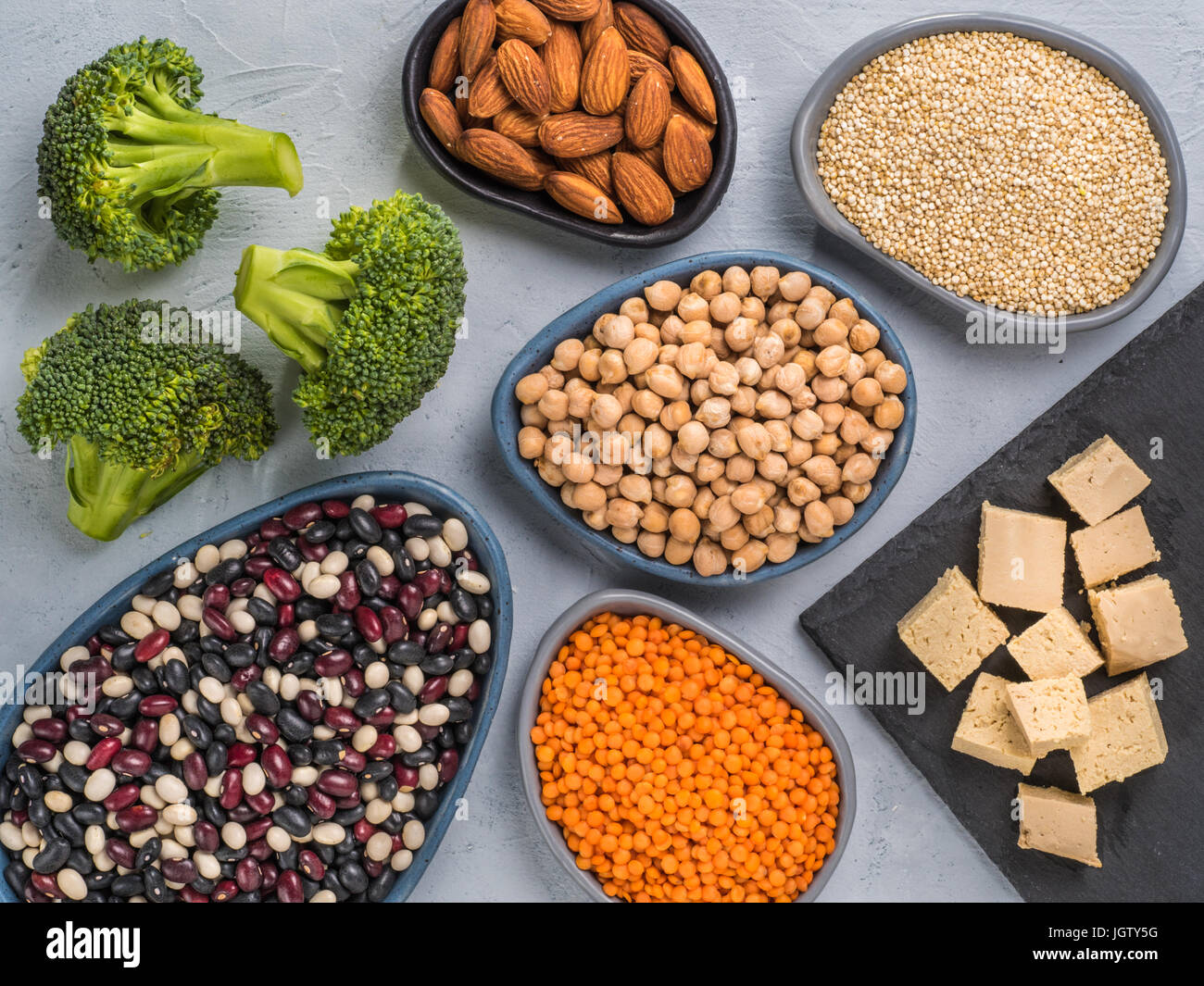 Vegetariano sano fonti di proteine sul cemento grigio Sfondo. La quinoa, ceci, mandorla, lenticchie rosse, misti bean, broccoli, tofu vegano come fonti di Foto Stock