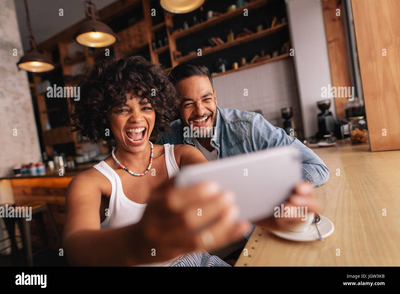 Felice coppia giovane seduto insieme al cafe e tenendo selfie utilizzando il telefono cellulare. Donna africana con il suo fidanzato tenendo autoritratto con smart pho Foto Stock