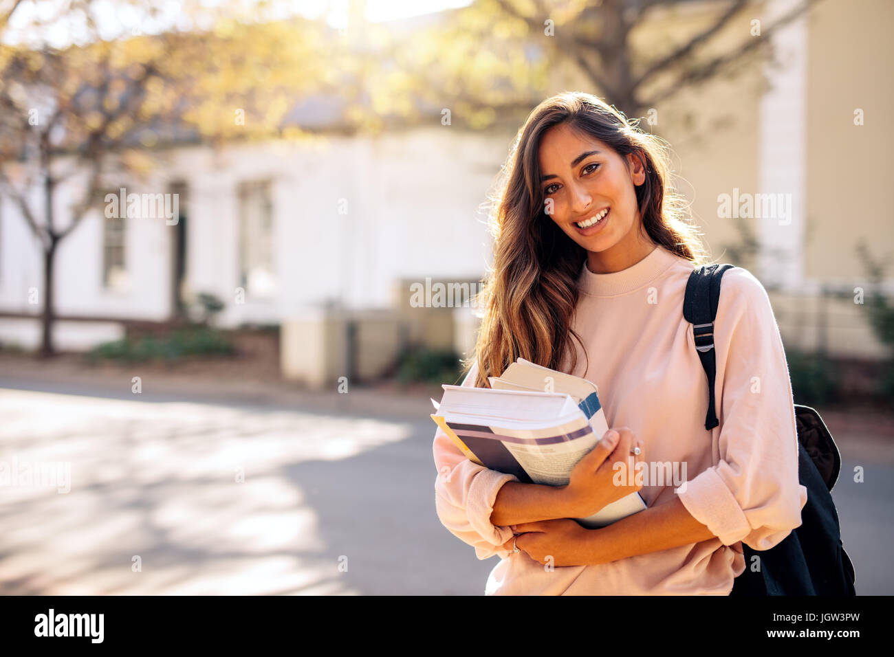 Bella giovane donna con zaino e libri all'esterno. Studente di college che porta un sacco di libri in college campus. Foto Stock