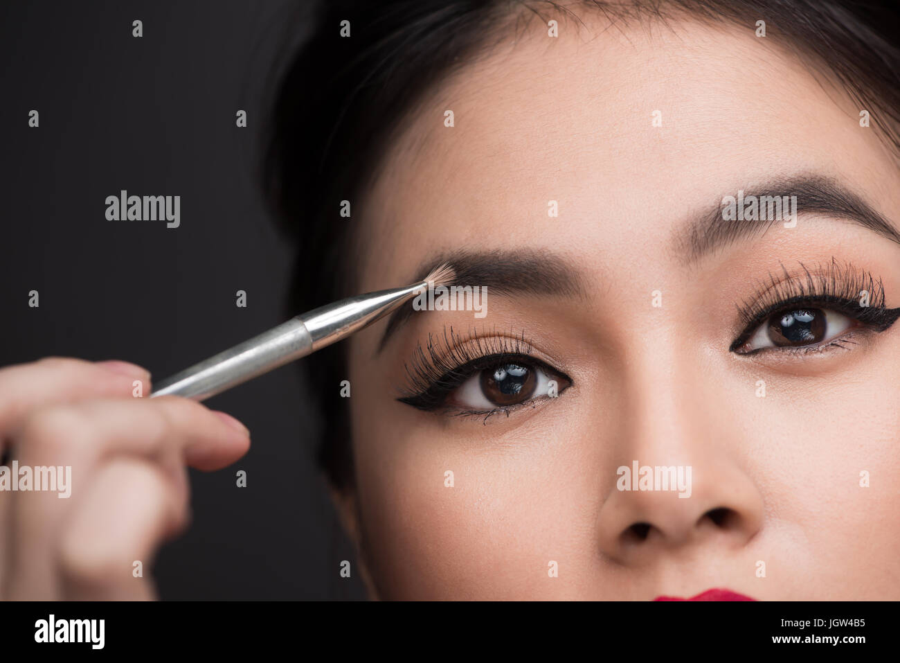 Vista ritagliata della donna asiatica con il trucco tenendo l'applicatore  mascara isolato su marrone, immagine stock Foto stock - Alamy