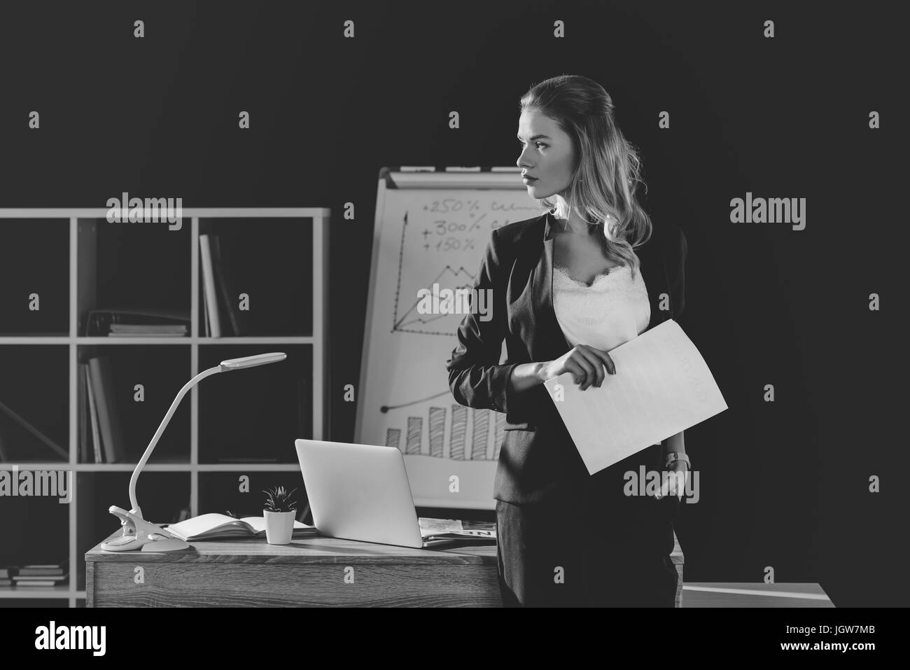 Attraente imprenditrice lavoro in ufficio, lavagna con grafici e tabelle dietro, in bianco e nero Foto Stock