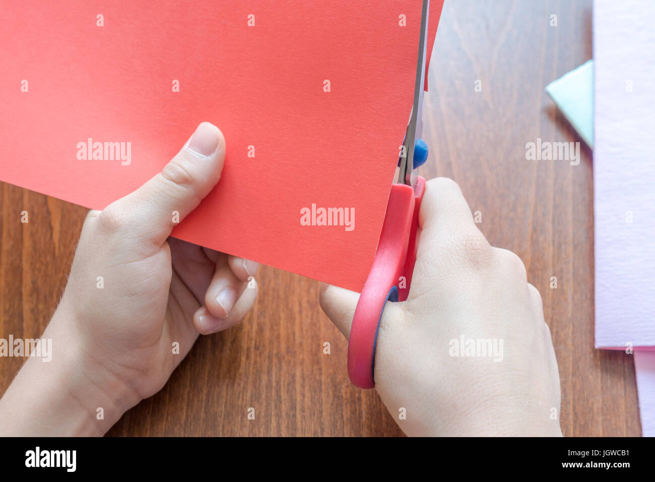 Bambino con le mani in mano il taglio colorato di rosso la carta con le forbici Foto Stock