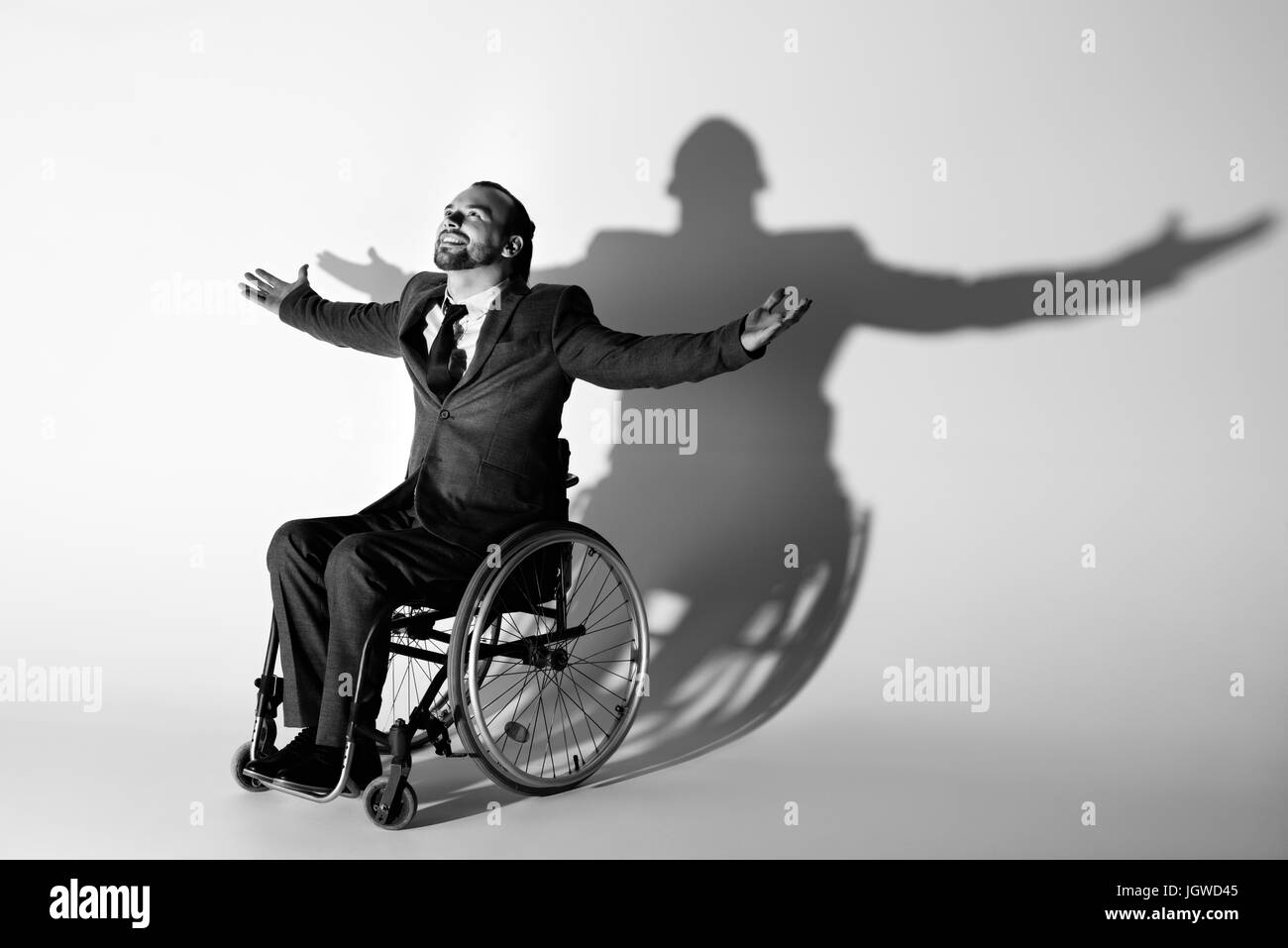 Allegro imprenditore nel soddisfare seduto nella sedia a rotelle gesticolando con ombra sul muro bianco, bianco e nero Foto Stock