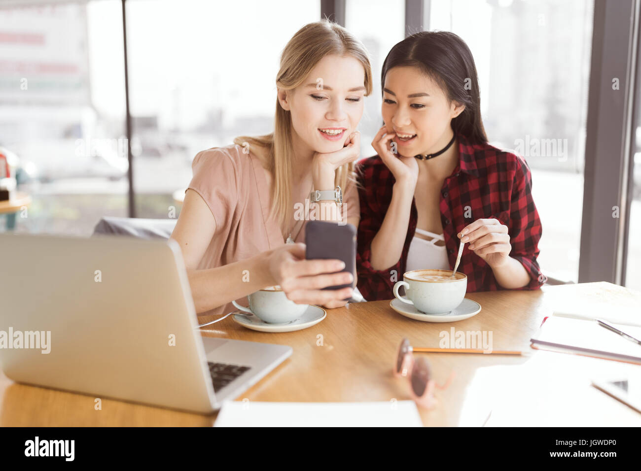 Sorridente giovani donne utilizza lo smartphone mentre si beve il caffè insieme all incontro a pranzo Foto Stock