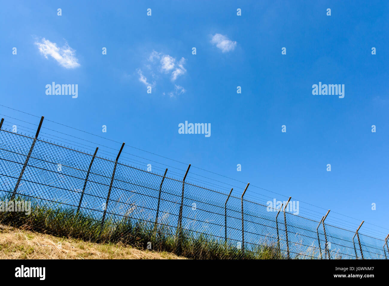 Una frontiera fatta di un doppio recinto di filo con filo spinato sulla sommità di una banca sotto un sole cocente e una summer blue sky. Foto Stock