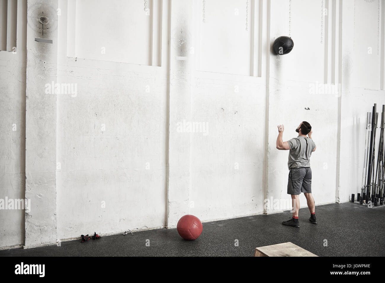 Uomo di gettare la sfera fitness contro la parete trasversale di palestra di formazione Foto Stock