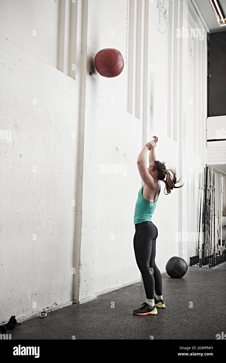 Donna fitness gettando la sfera contro la parete trasversale di palestra di formazione Foto Stock