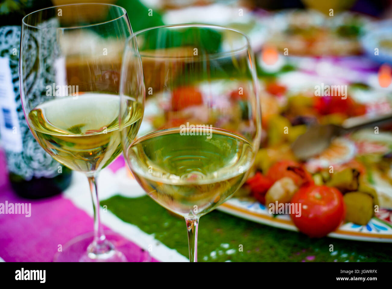 Due metà riempito bicchieri di vino a tavola il cibo sulla piastra dietro, close-up Foto Stock