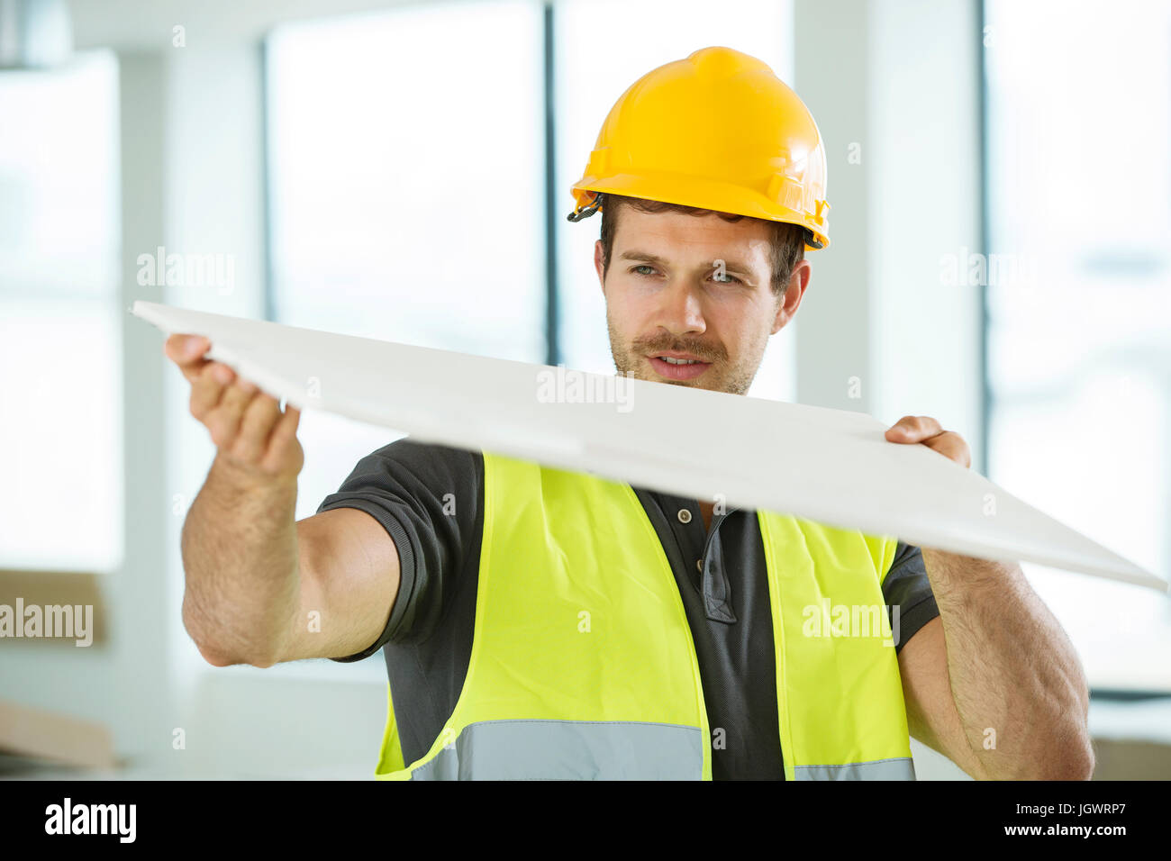 Uomo che indossa hi vis vest, in piedi nel nuovo spazio costruito, guardando il materiale di costruzione Foto Stock
