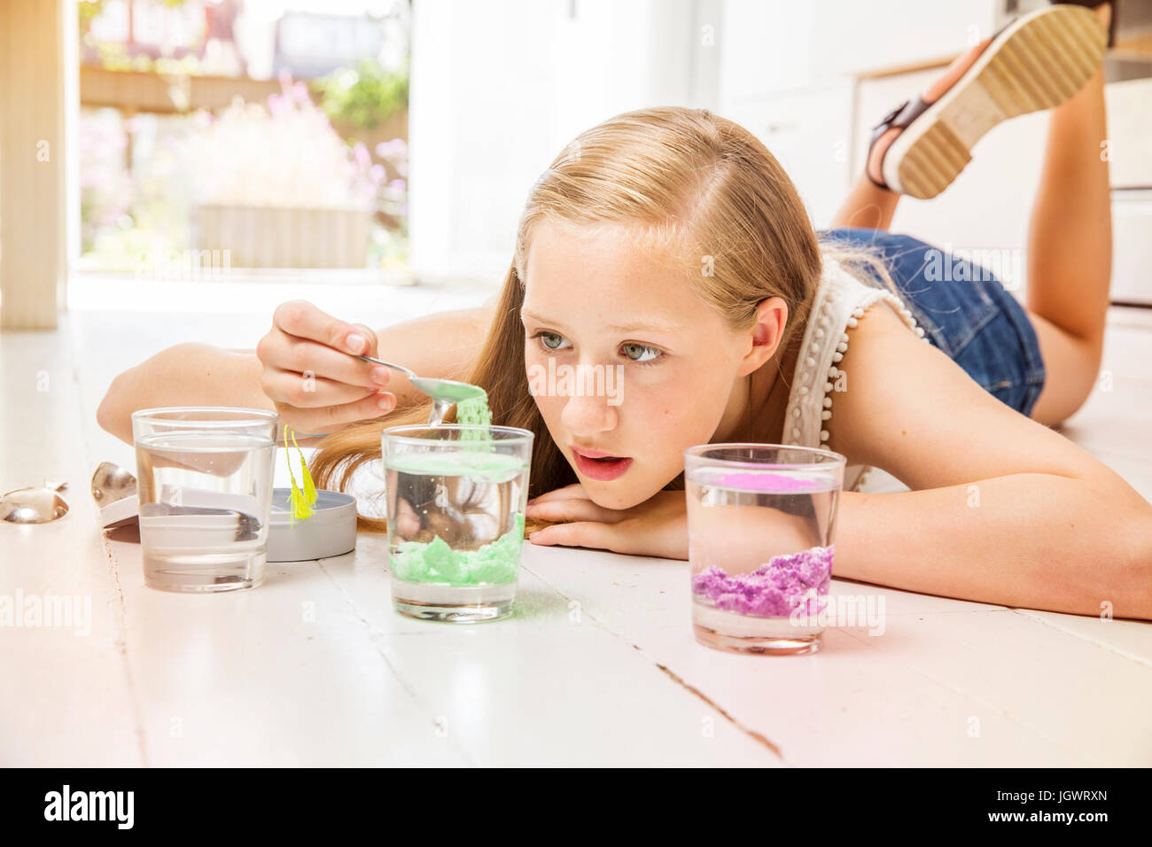 Ragazza distesa sul pavimento facendo esperimento con bicchieri di acqua Foto Stock