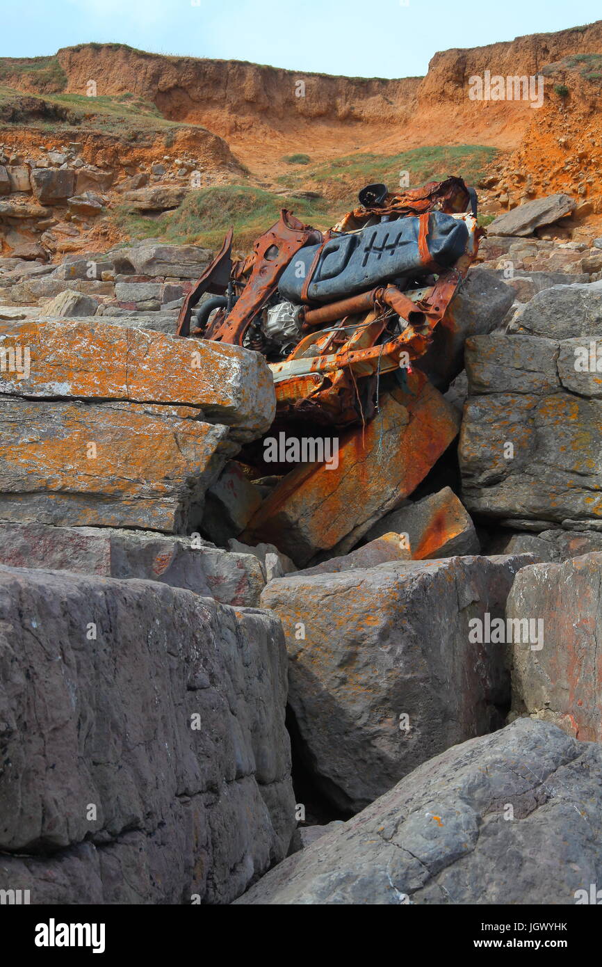 Guardando verso la parte superiore di una piccola scogliera è il mangled relitto di una spiaggia Buggy si incunei saldamente in una crepa di pietra appena al di sopra della high water mark. Foto Stock