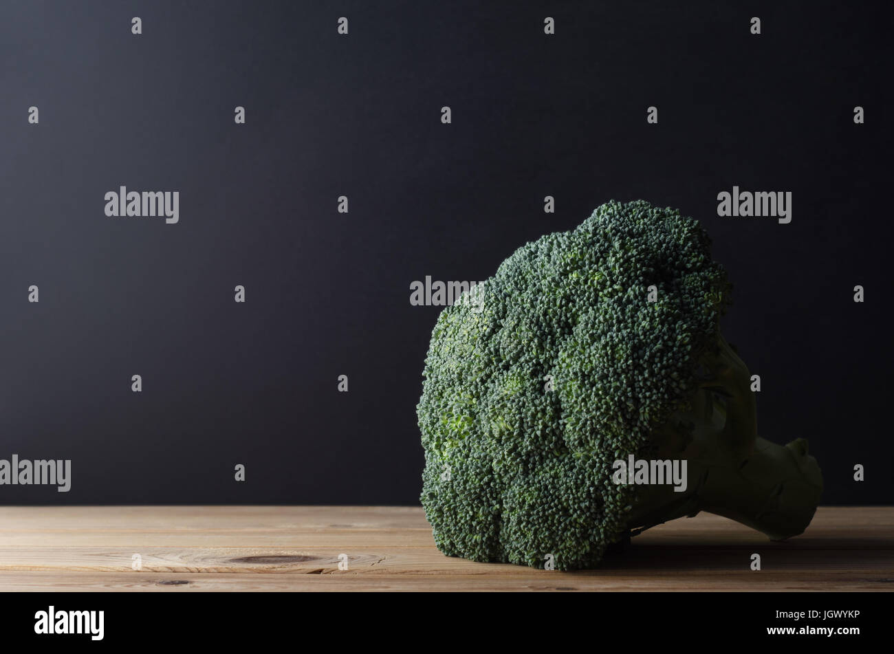 Una testa di colore verde scuro con broccoli peduncolo intatto, su planked in legno tavolo da cucina contro la lavagna nera dello sfondo. Moody illuminazione. Foto Stock