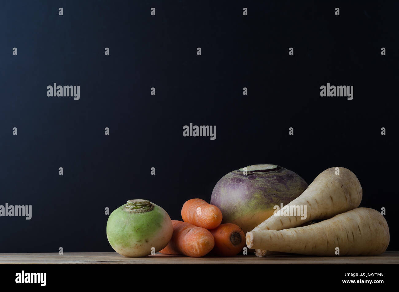 Ancora vita disposizione degli ortaggi a radice (rapa, carote, svedese e pastinaca) su un legno planked tabella con una lavagna in soft focus sfondo per Foto Stock