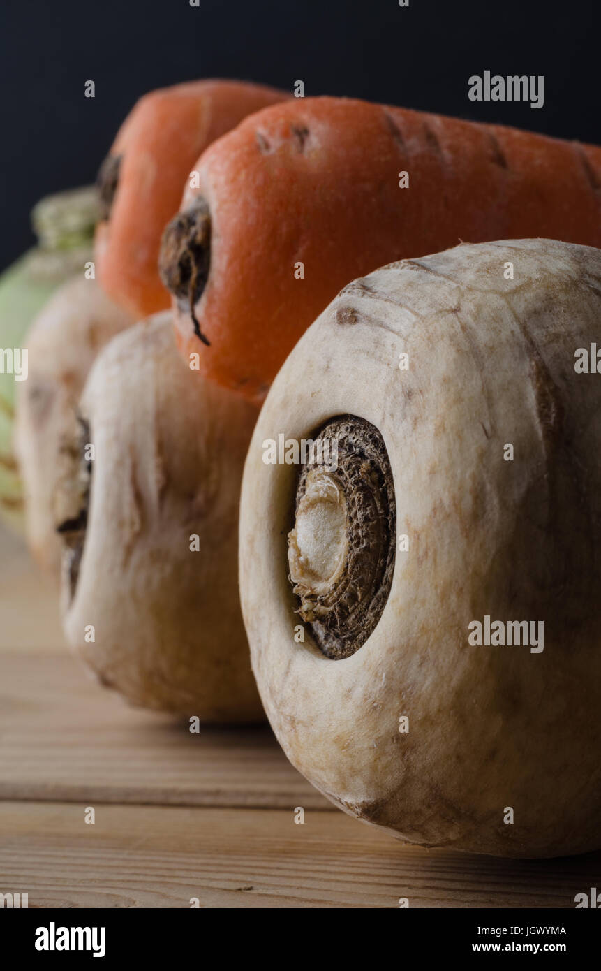 Una chiusura selezione di unwashed ortaggi a radice - pastinaca; carote e rape - in una fila che conduce in background su un legno planked tavolo da cucina. B Foto Stock