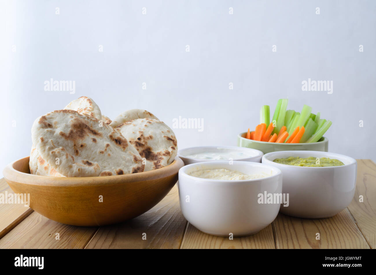 Una selezione di ribassi su un asse di legno tabella, con le ciotole di pane pitta e crudites. Include; hummus; guacamole; formaggio ed erba cipollina, il sedano e la carota. Foto Stock