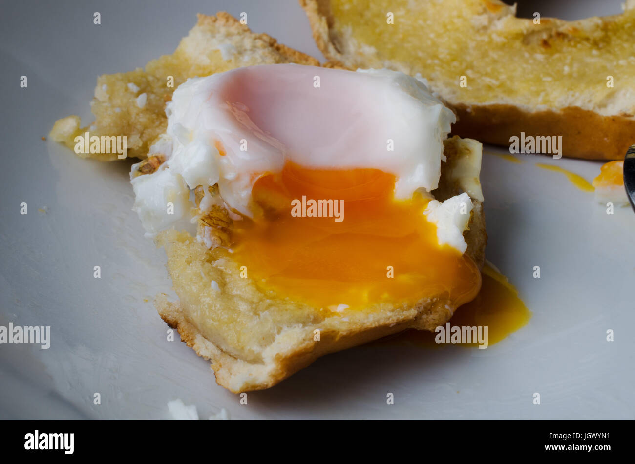 Close up di un parzialmente consumato senza intervallo uovo fritto a tostare bagel con tuorlo d'uovo trafili oltre il bordo. Metà rimanente bagel in background. Foto Stock