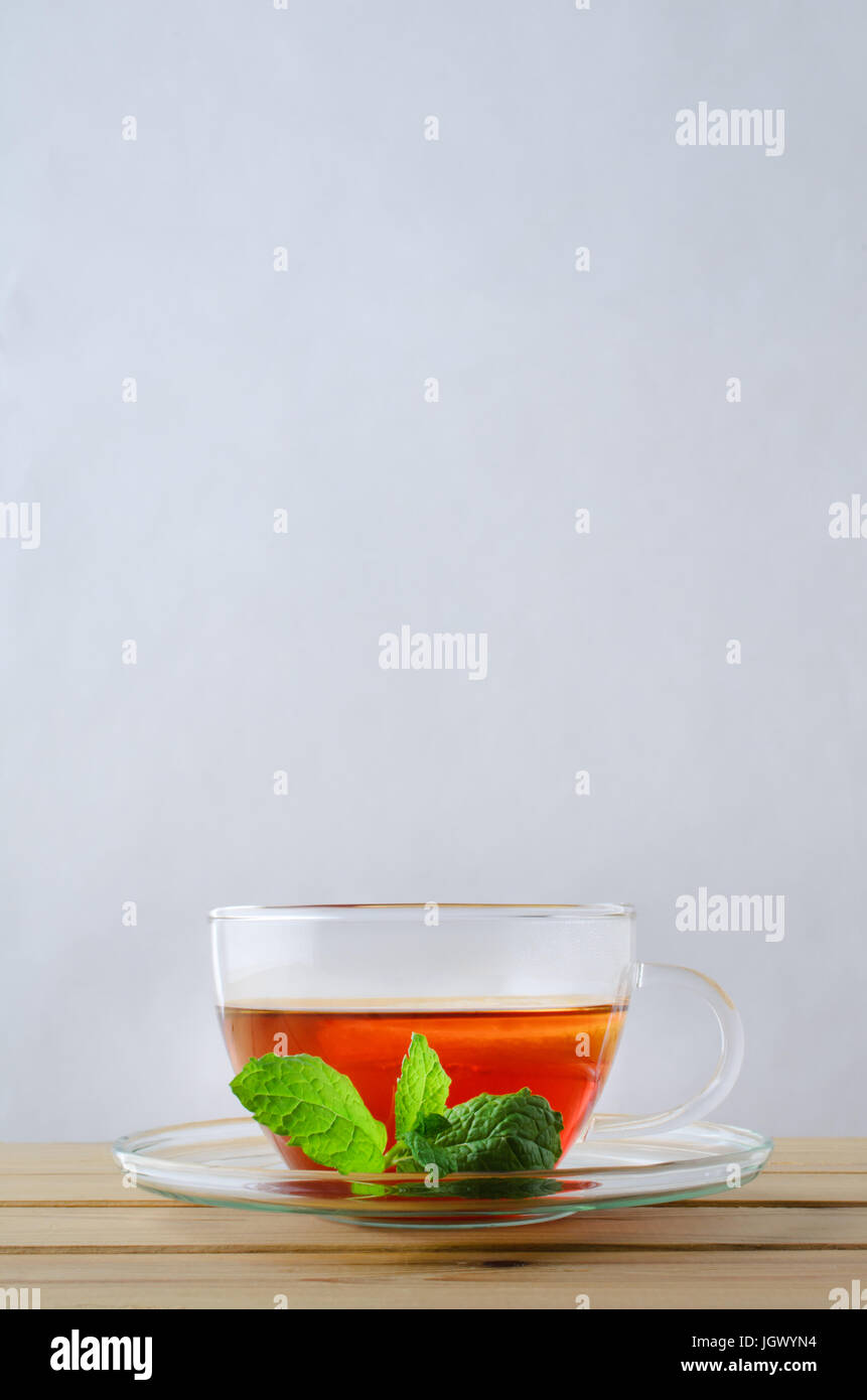Colpo verticale di una coppa di vetro contenente il tè con una fetta di limone su un tavolo di legno. Un rametto di foglie di menta in appoggio sul piattino. Copia spazio sopra. Foto Stock