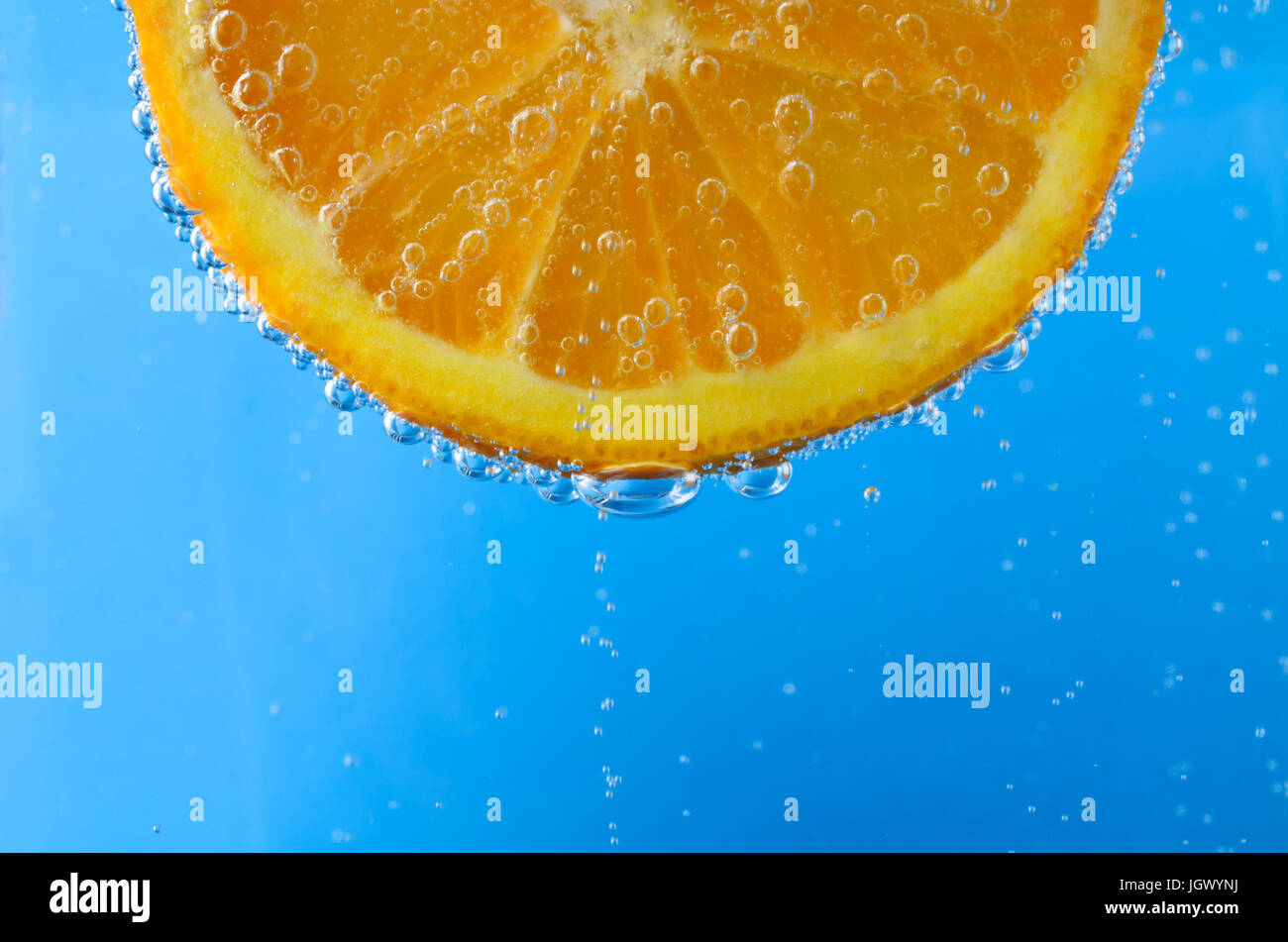 In prossimità di una fresca fetta di colore arancione nella parte superiore dell'immagine e rivolto in avanti, sospeso in brillante acqua blu. Bolle di ossigeno la flottazione verso l'alto e cove Foto Stock