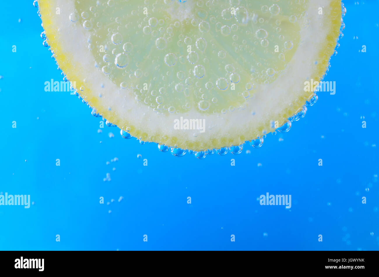 Close up di un taglio fresco fetta di limone sulla parte superiore dell'immagine e rivolto in avanti, sospeso in brillante acqua blu. Bolle di ossigeno la flottazione verso l'alto e Foto Stock