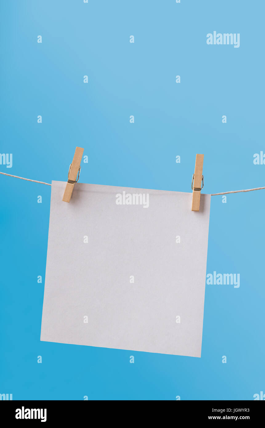Un singolo foglio di bianco, quadrato di carta, pendente da una linea di abbigliamento su picchetti di legno contro un cielo blu chiaro. Lasciato vuoto per copiare lo spazio. Foto Stock