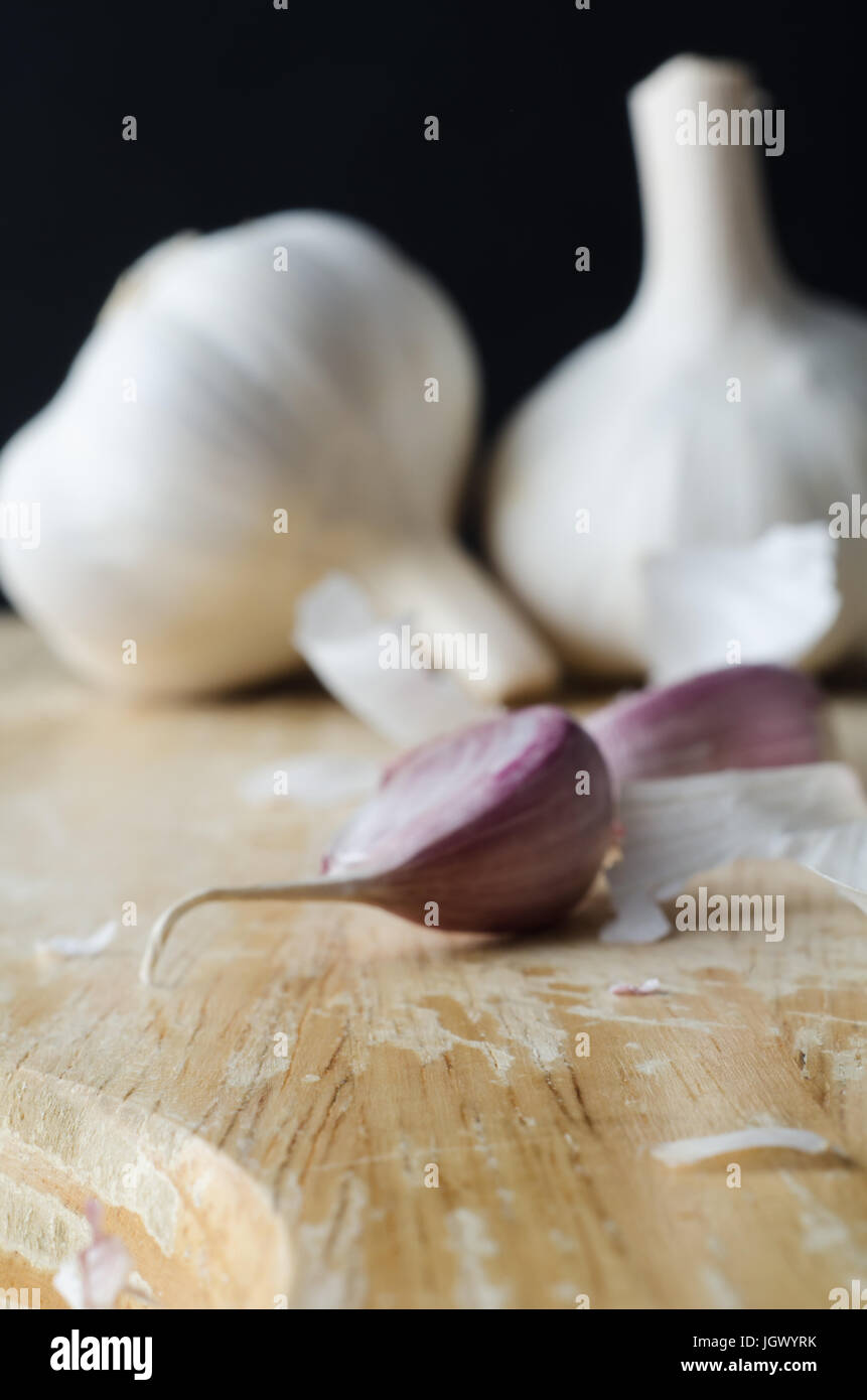 Due interi bulbi di aglio in background, con chiodi di garofano rosa in primo piano su un tagliere di legno circondato da sparsi frammenti di shredded pap Foto Stock