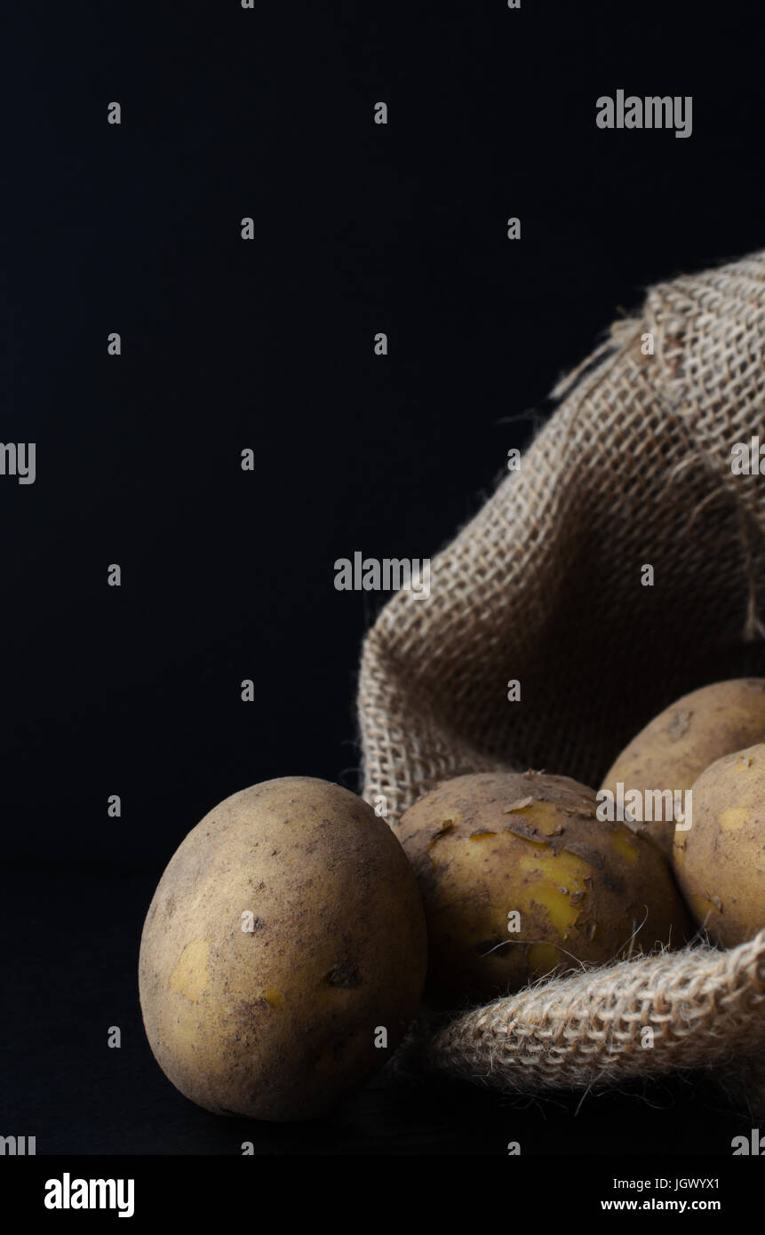 Materie, non lavate e con la buccia di patate, la fuoriuscita del sacco di Hesse. Moody illuminazione, la superficie nera e lo sfondo. Foto Stock