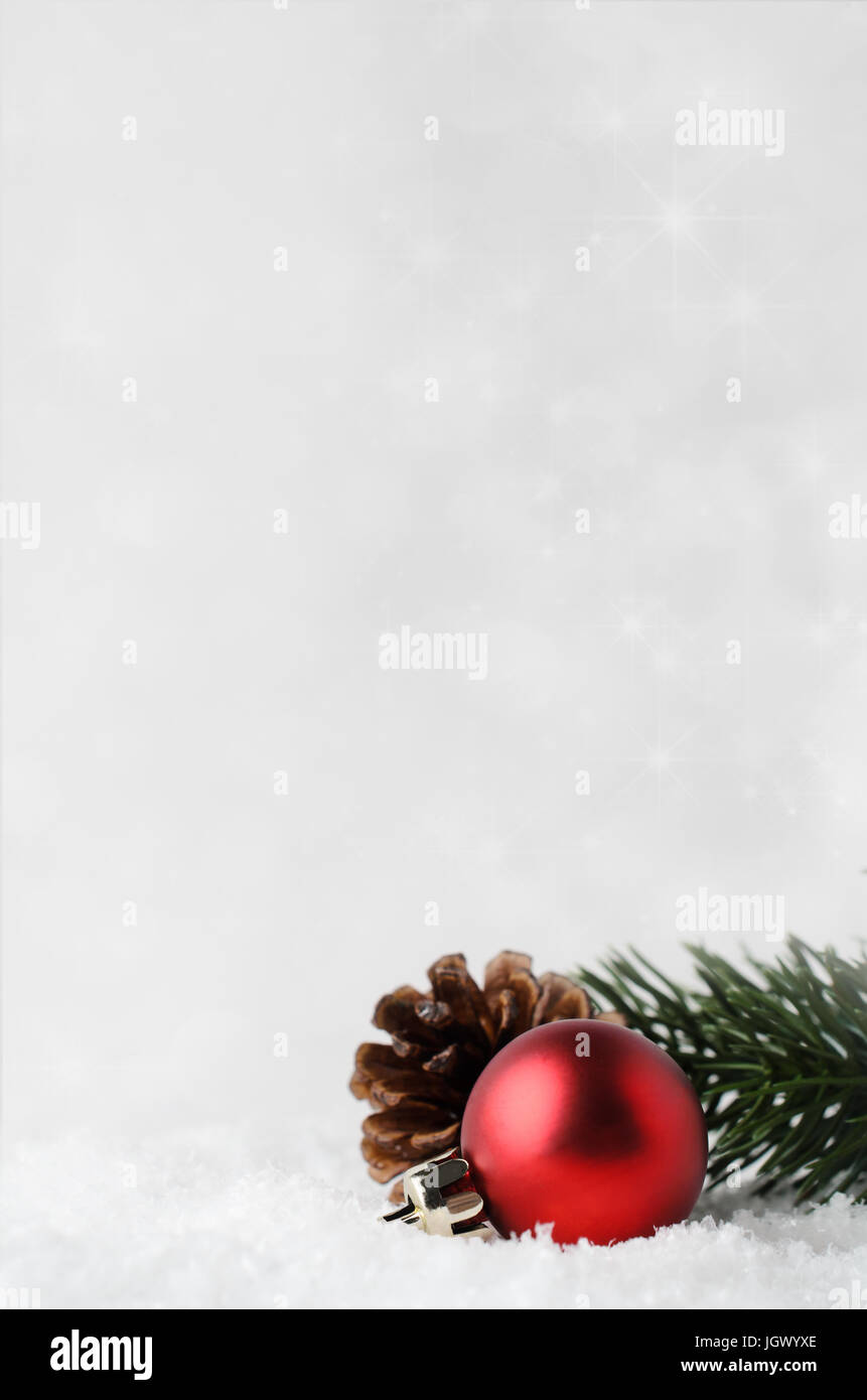 Un Natale di confine e con sfondo rosso ninnolo, fir cono e ramo verde, immerso nel bianco della neve falsa nell'angolo inferiore destro. Stelle scintillanti in b Foto Stock