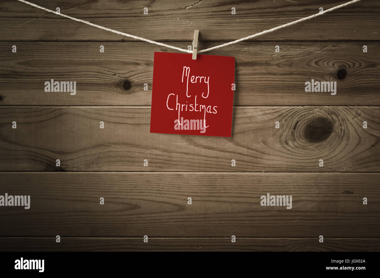 Buon Natale messaggio manoscritta su una piazza di festosa nota rossa carta e ancorato a una stringa linea di lavaggio. Asse di legno con uno sfondo saturat bassa Foto Stock
