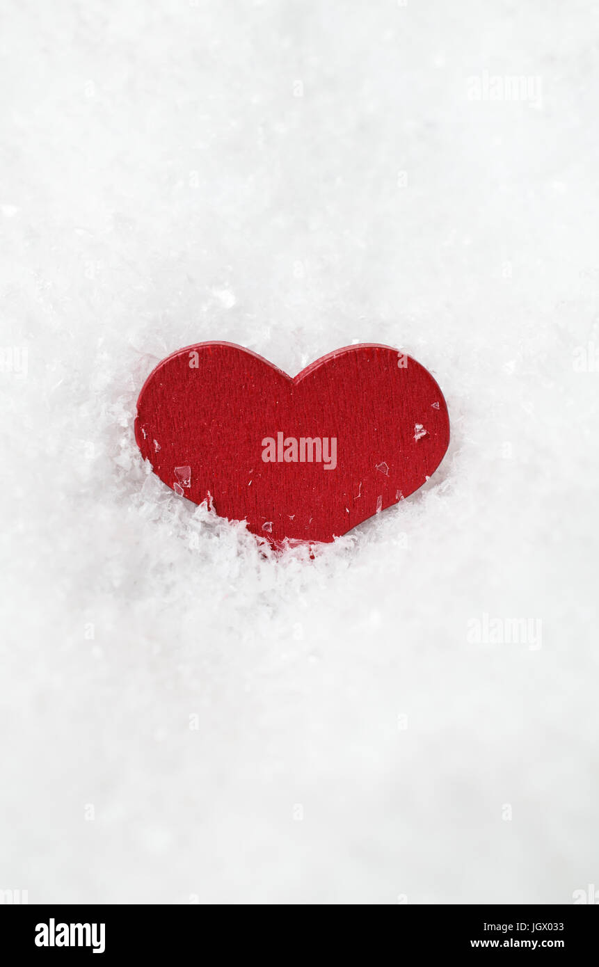 Un rosso cuore di legno, parzialmente sommerso in bianco neve artificiale, centrata verticalmente con copia di spazio al di sopra e al di sotto. Foto Stock