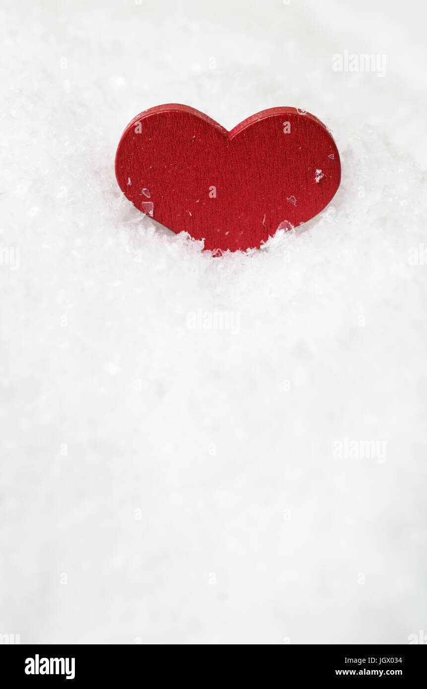Un rosso cuore di legno, verticale e accoccolato in artificiale bianco della neve nella sezione superiore del telaio con copia spazio sottostante. Foto Stock
