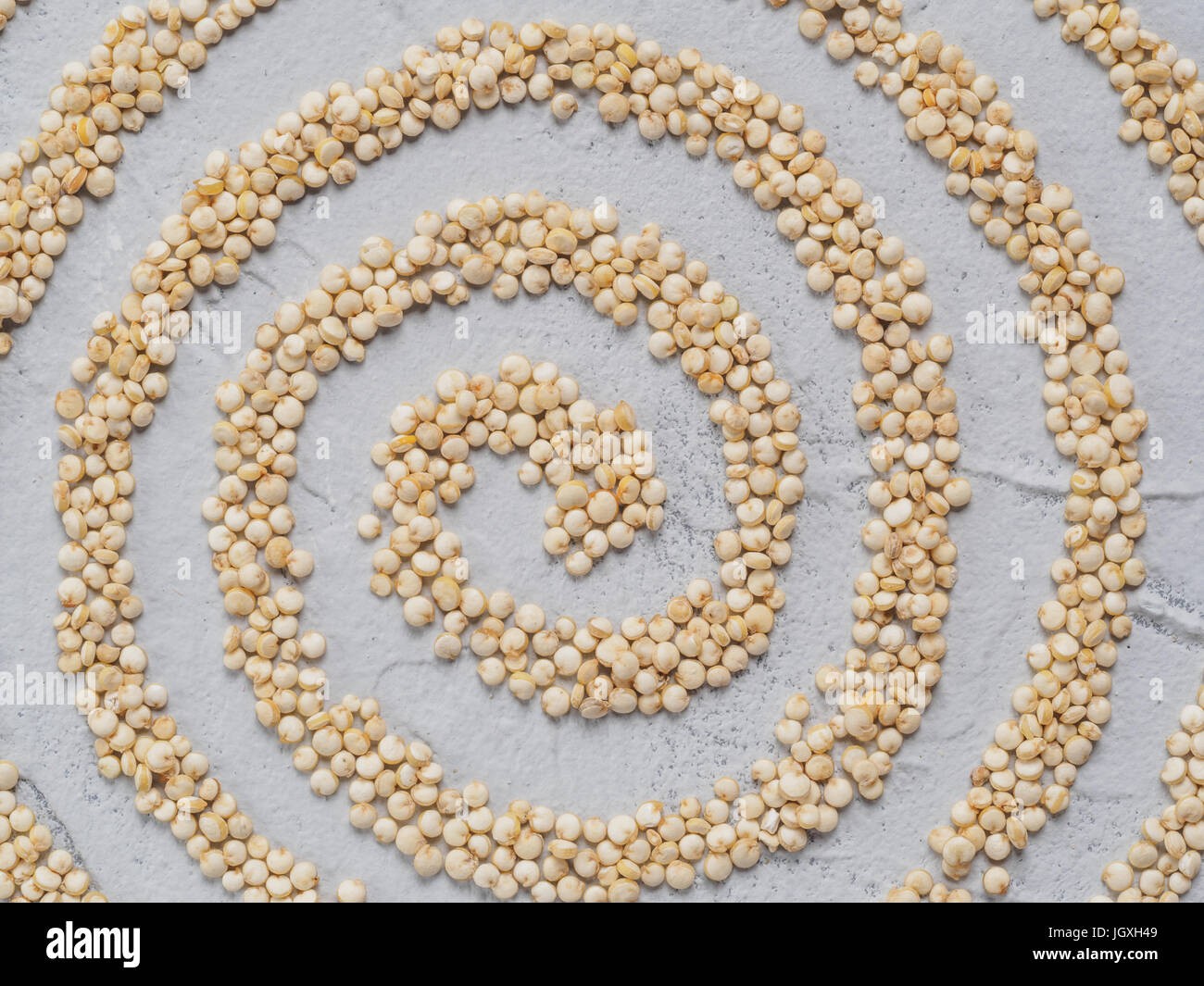 Grano di quinoa. Non cotti materie quinoa spirale astratta, giacente sul cemento grigio Sfondo. Sano cibo vegan concetto e pattern. Vista superiore o laici piatta Foto Stock