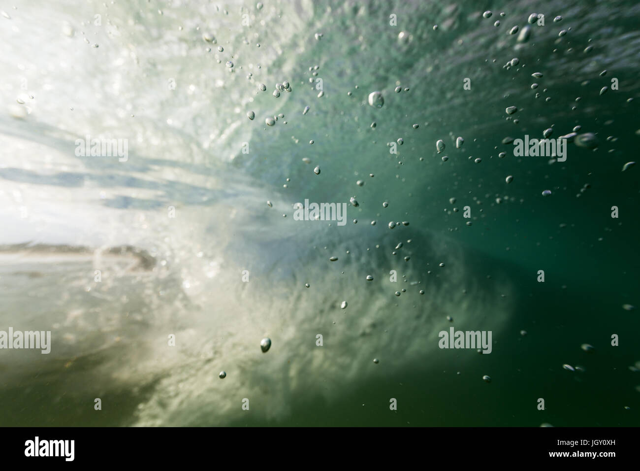 Le bollicine salgono in chiaro l'acqua dell'oceano dal mare piano in questa ripresa subacquea come un'onda passa in background. Foto Stock