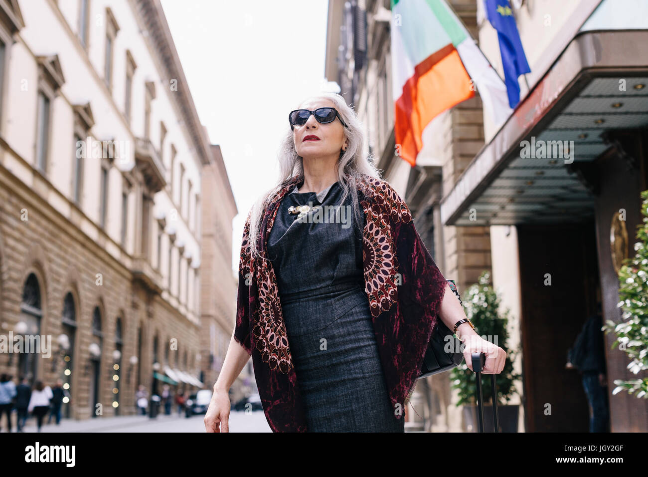 Donna matura con lunghi capelli grigi con valigia trolley fuori dall'hotel a Firenze, Italia Foto Stock