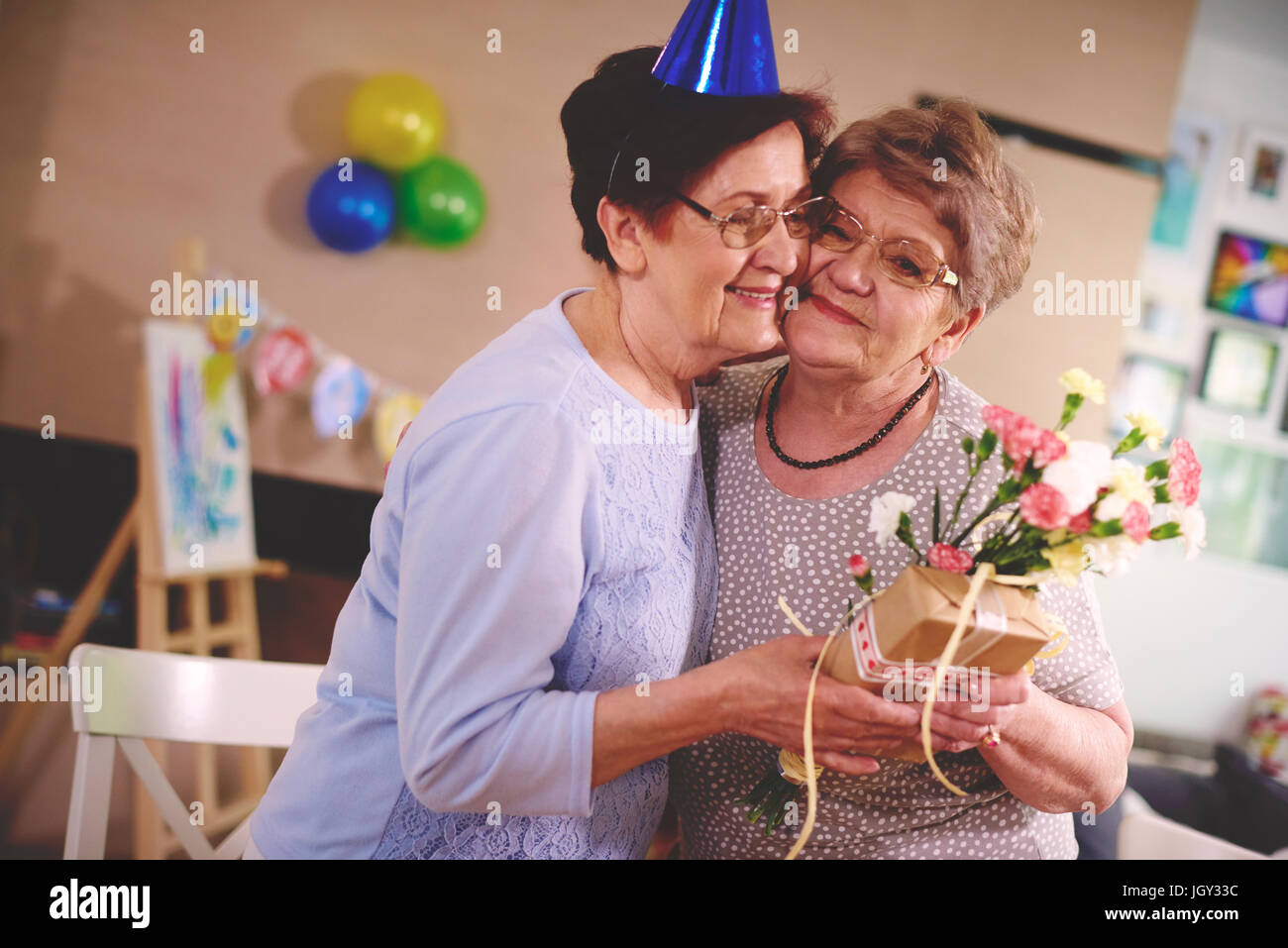 Senior donna fiori dando ad un amico alla festa di compleanno Foto Stock