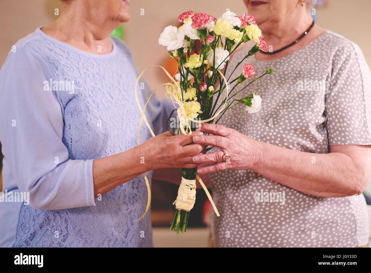 Senior donna fiori dando ad un amico alla festa di compleanno Foto Stock