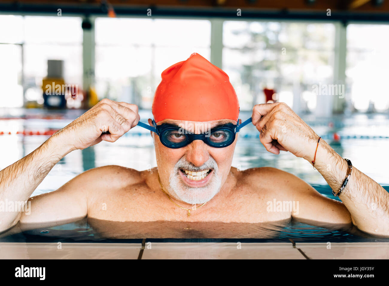Senior uomo tirando significa affrontare indossare gli occhiali di protezione in piscina Foto Stock