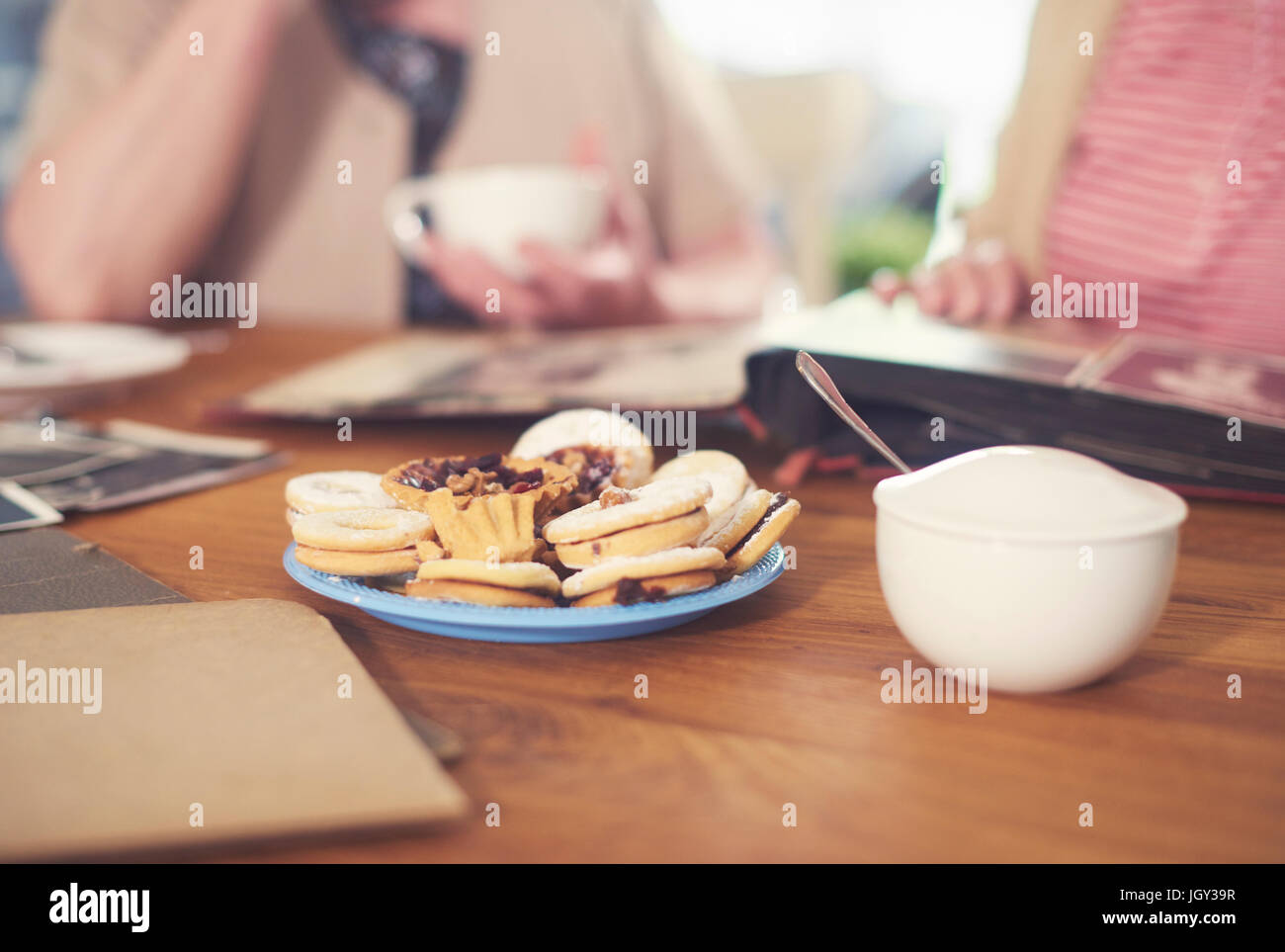 Ritagliato colpo di senior donne a tavola con zuccheriera, biscotti e album di foto Foto Stock