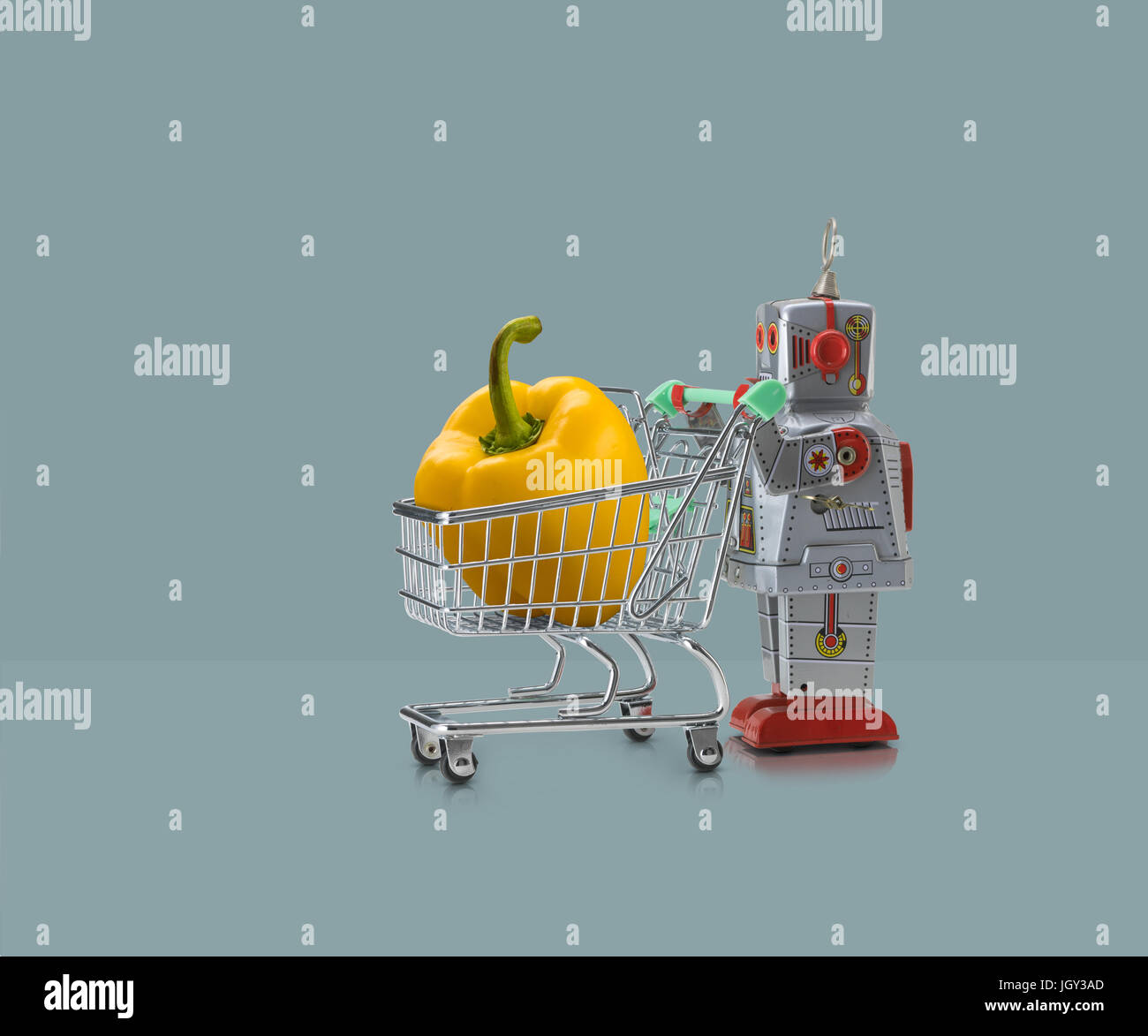 Robot giocattolo in miniatura di spinta carrello della spesa con il peperone giallo contro sfondo blu Foto Stock