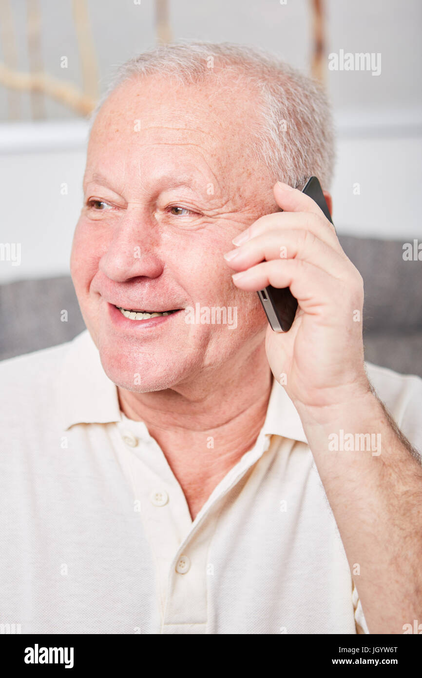 Senior con lo smartphone ascolta con attenzione e la gioia di un messaggio Foto Stock