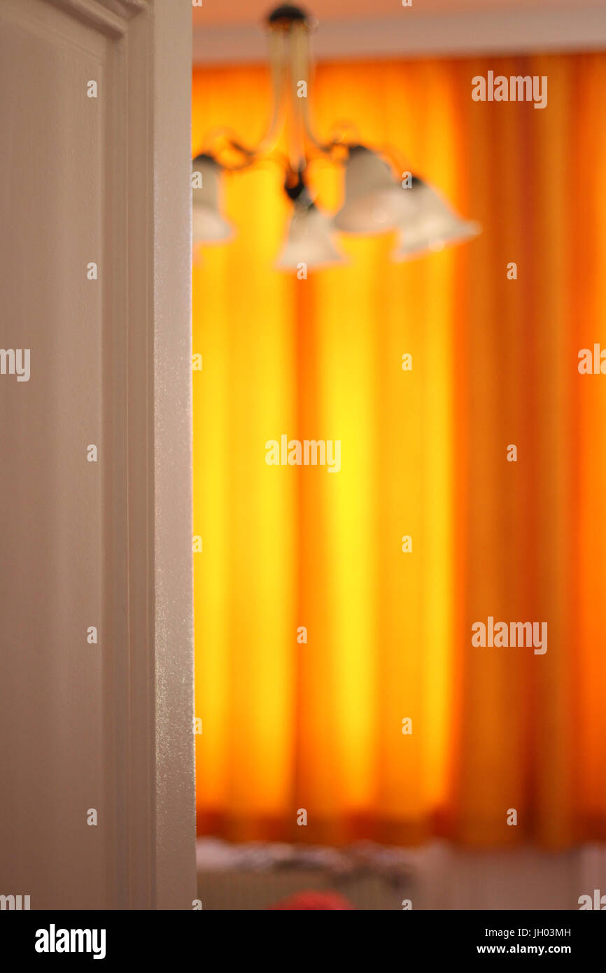 Una camera in un vecchio edificio con tende di colore arancione e una lampada a soffitto Foto Stock