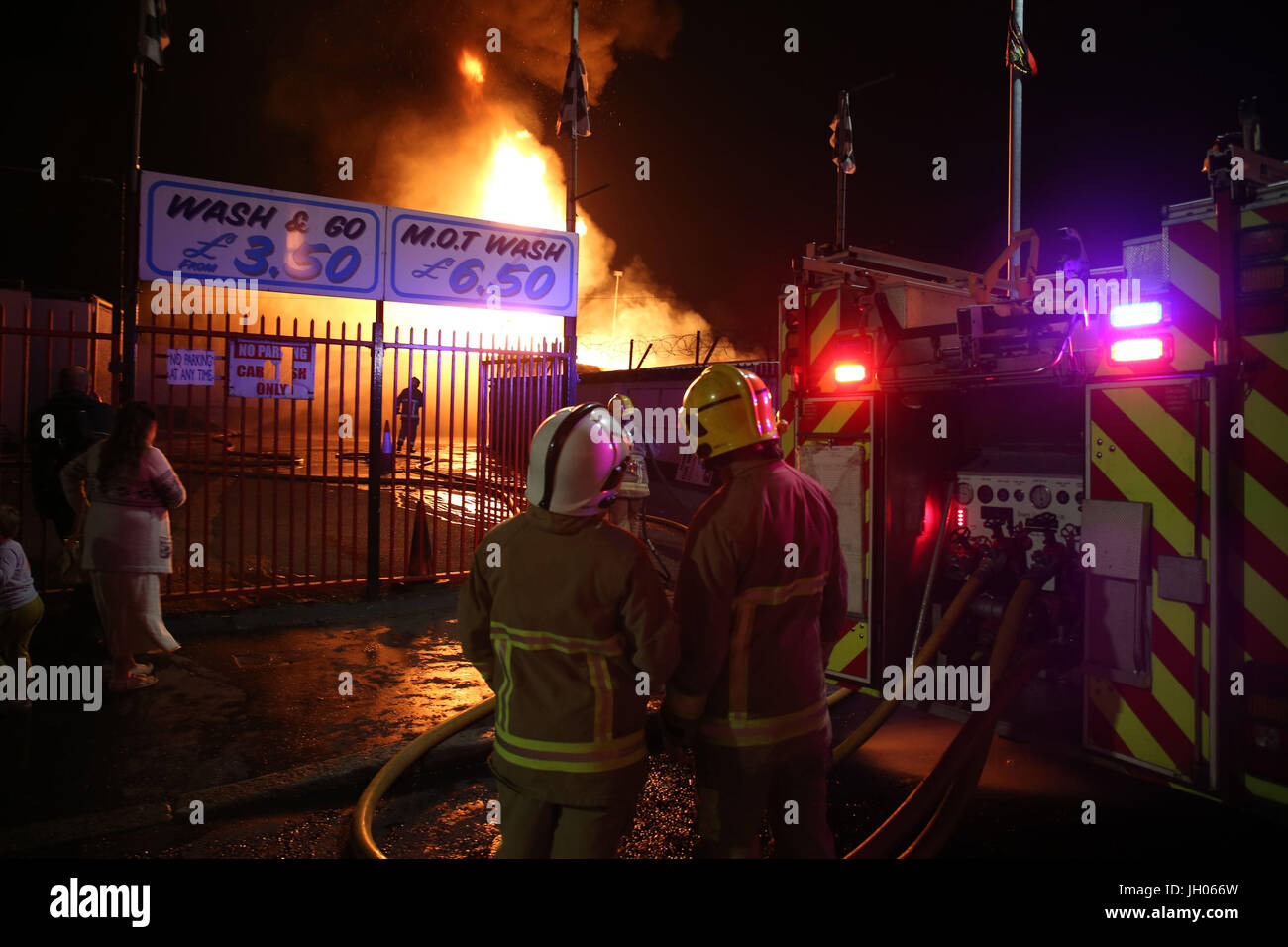 Vigili del fuoco smorzare vicino casa come un falò a Ravenscroft Avenue a Belfast è accesa prima della data chiave nella protestante ordine leale marching stagione - il dodicesimo di luglio. Foto Stock